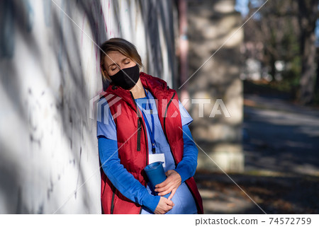 Tired woman caregiver or healthcare worker having a break outdoors, coronavirus concept. Tired woman caregiver or healthcare worker having a break outdoors, coronavirus concept. 74572759