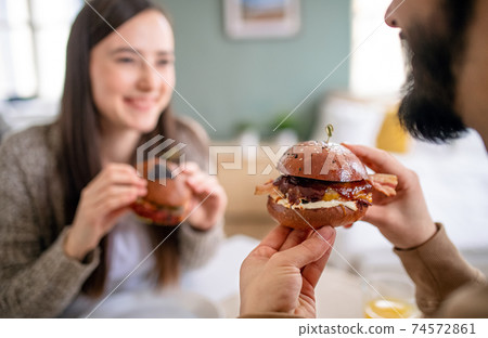Unrecognizable young couple in love eating hamburgers indoors at home. 74572861