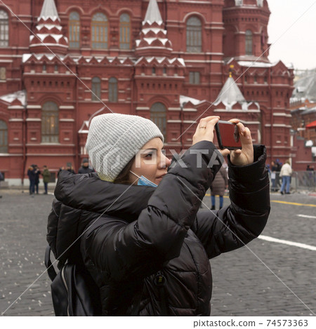 A young she tourist on Red Square in Moscow shoots architecture on a smartphone 74573363