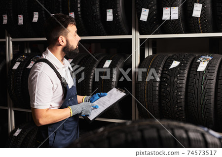 european male Mechanic holding paper tablet document in hands while checking the assortment in car repair service european male Mechanic holding paper tablet document in hands while checking the assortment in car repair service 74573517