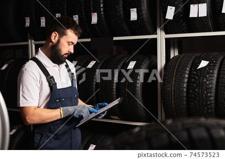 european male Mechanic holding paper tablet document in hands while checking the assortment in car repair service european male Mechanic holding paper tablet document in hands while checking the assortment in car repair service 74573523