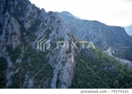 Close up of a mountain range with green trees over the road. 74574101