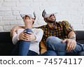Young Couple Playing Virtual Reality With Headset On Sofa 74574117