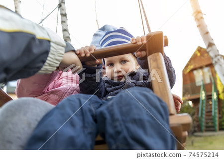 Two cute adorable playful caucasian siblings boy girl child enjoy having fun swinging wooden swing at backyard together with father. Little toddler brother and sister laughing at playing outdoors Two cute adorable playful caucasian siblings boy girl child enjoy having fun swinging wooden swing at backyard together with father. Little toddler brother and sister laughing at playing outdoors 74575214