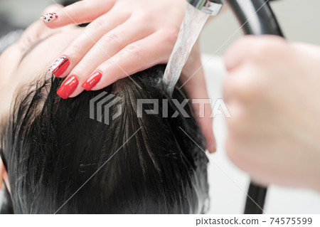Hands of hairstylist wash hair of brunette with shampoo in professional sink for shampooing in beauty salon 74575599