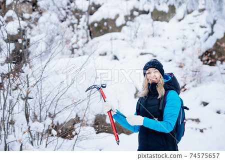 Happy, smiling mountaineer with an ice ax in hand in a beautiful winter scenery in the mountains. 74575657