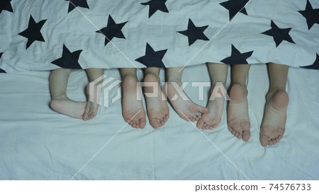 Legs of babies in the bed from under the covers before going to bed. 74576733