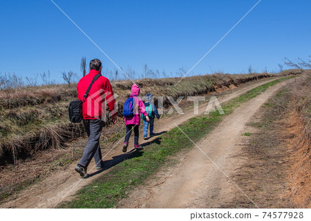 Father with children is walking along the path in boots and with backpacks. 74577928