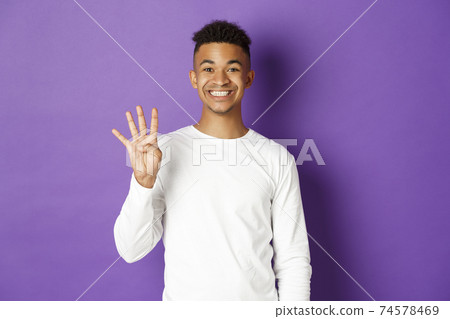 Image of cheerful african-american guy in white sweatshirt, showing number four and smiling, standing over purple background Image of cheerful african-american guy in white sweatshirt, showing number four and smiling, standing over purple background 74578469
