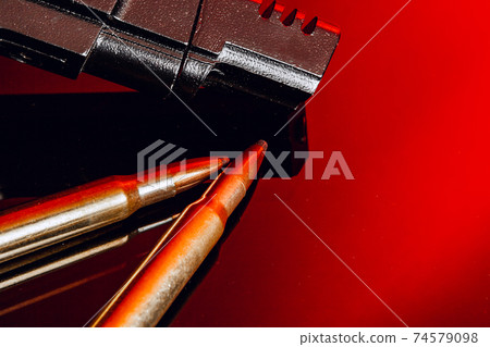 Black gun and cartridges on background with red reflection Black gun and cartridges on background with red reflection 74579098