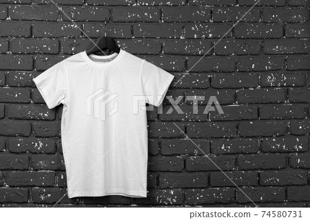 White t-shirt hanging on hanger against brick wall White t-shirt hanging on hanger against brick wall 74580731