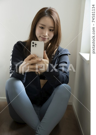 一個女人看著運動服的智能手機 74581134