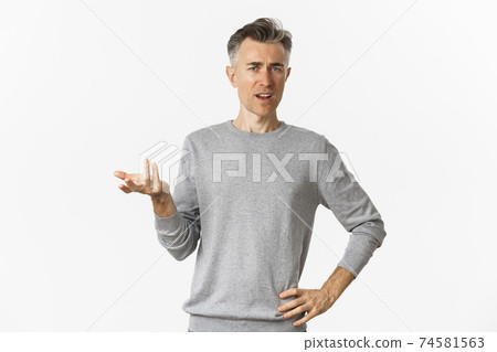 Portrait of confused and disappointed middle-aged man, pointing at something strange and looking at camera, waiting for explanation, standing over white background Portrait of confused and disappointed middle-aged man, pointing at something strange and looking at camera, waiting for explanation, standing over white background 74581563