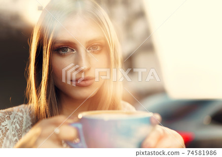 Portrait of a young woman having a cup of coffee and looking through the window Portrait of a young woman having a cup of coffee and looking through the window 74581986