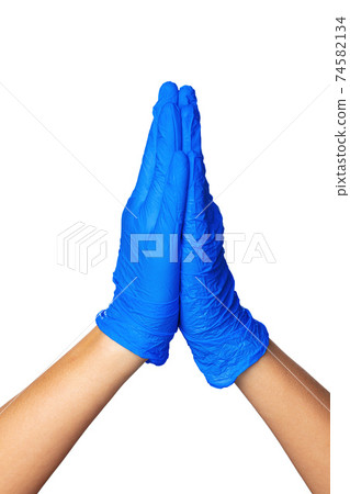 Hands in blue latex medical gloves folded together indicating the process of prayer. 74582134