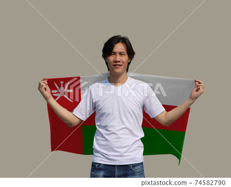The man holding Oman fabric flag on his shoulder on grey background. 74582790
