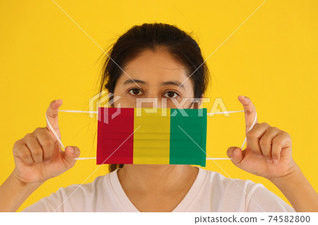 A woman in white shirt with Guinea flag on hygienic mask in her hand and lifted up the front face A woman in white shirt with Guinea flag on hygienic mask in her hand and lifted up the front face 74582800