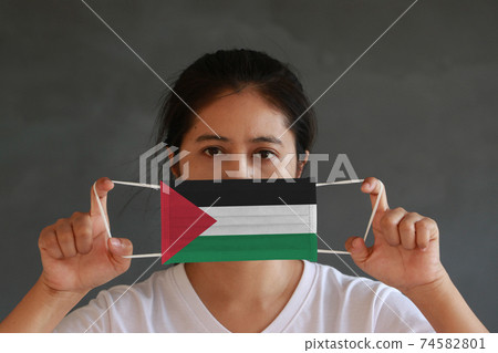 A woman in white shirt with Palestine flag on hygienic mask in her hand and lifted up the front face A woman in white shirt with Palestine flag on hygienic mask in her hand and lifted up the front face 74582801