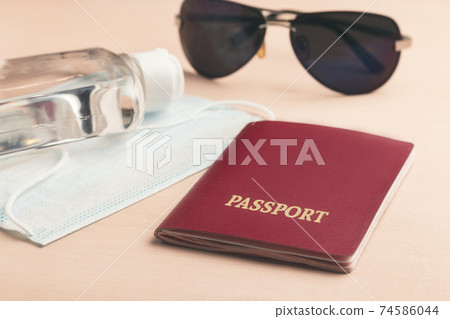 Safe travel during coronavirus pandemic concept. Protective medical mask, sunglasses, sanitizer and passport on the table Safe travel during coronavirus pandemic concept. Protective medical mask, sunglasses, sanitizer and passport on the table 74586044