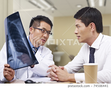 asian doctor talking to patient about x-ray result asian doctor talking to patient about x-ray result 74586441