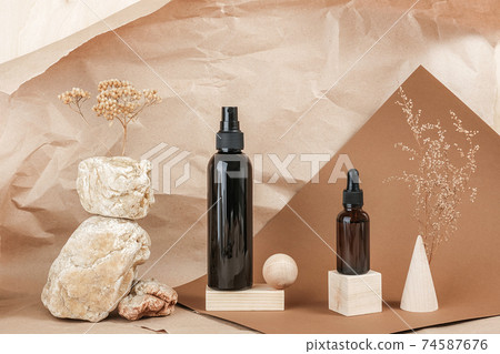 Brown glass bottles of cosmetic products on stone, wooden geometric shapes and dry flowers on beige paper background. Natural Organic Spa Cosmetic Beauty concept Front view Mockup 74587676