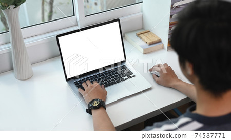 A young asian man using computer laptop browsing surfing internet at home. 74587771