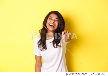 Portrait of beautiful and happy african-american woman laughing, pointing finger at you, found excellent candidate, standing over yellow background Portrait of beautiful and happy african-american woman laughing, pointing finger at you, found excellent candidate, standing over yellow background 74588182