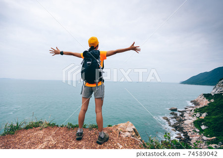 Successful hiker outstretched arms at seaside mountain top cliff edge 74589042