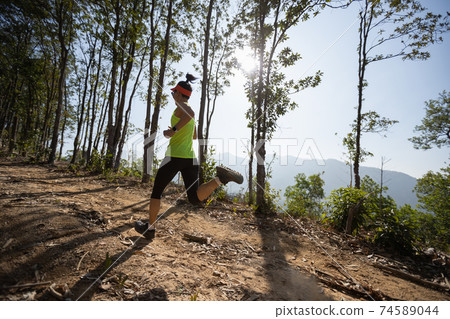 Young woman trail runner running in sunrise tropical forest 74589044