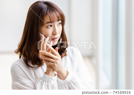 A woman who puts her smartphone on her ear and shows an annoying expression A woman who puts her smartphone on her ear and shows an annoying expression 74589916