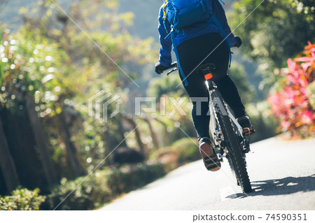 Woman riding a bike on tropical park trail in spring Woman riding a bike on tropical park trail in spring 74590351