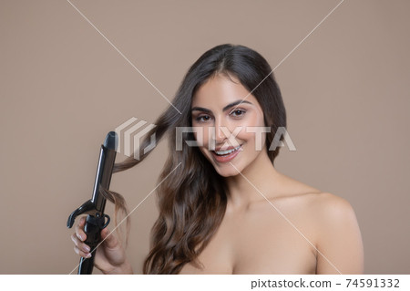 Woman holding strand of hair in curling iron Woman holding strand of hair in curling iron 74591332