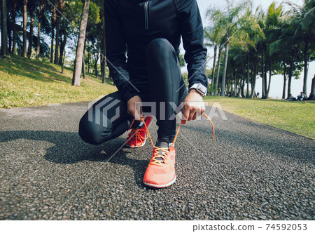Woman runner tying shoelace on sunny tropical park trail Woman runner tying shoelace on sunny tropical park trail 74592053