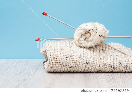 Woolen pullover and yarn for knitting. Skeins of natural wool yarn and knitting needles 74592219