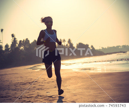 Young fitness woman running at sunrise beach 74593743