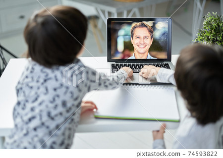 Online way. Happy male teacher smiling to his little students during online lesson for kids. Two hispanic boys using laptop while sitting at the table. Focus on laptop screen Online way. Happy male teacher smiling to his little students during online lesson for kids. Two hispanic boys using laptop while sitting at the table. Focus on laptop screen 74593822