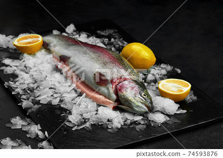 Raw fresh organic dorado or sea bream with lemon on ice cubes over black slate, stone or concrete background. Raw fresh organic dorado or sea bream with lemon on ice cubes over black slate, stone or concrete background. 74593876