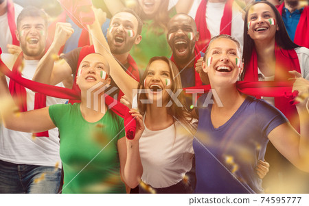Italian football, soccer fans cheering their team with a red scarfs at stadium. Excited fans cheering a goal, supporting favourite players 74595777