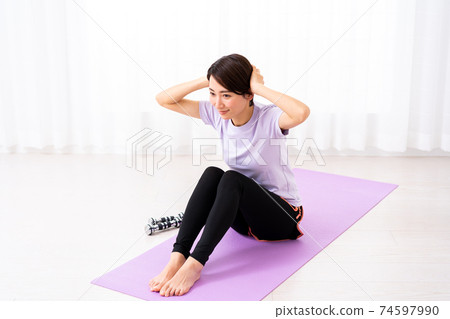 Middle-aged woman training abs in the living room at home Middle-aged woman training abs in the living room at home 74597990