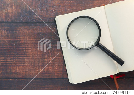 open book and magnifying glass on table. open book and magnifying glass on table. 74599114