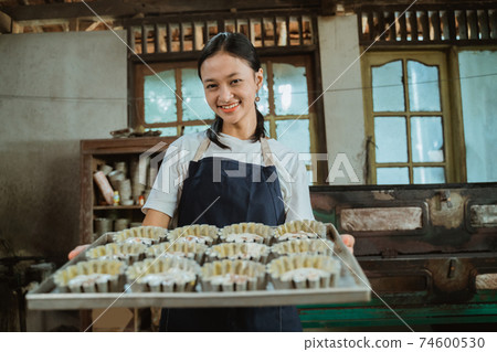 Close up of Asian girl carrying a baking sheet filled with several small cake molds Close up of Asian girl carrying a baking sheet filled with several small cake molds 74600530