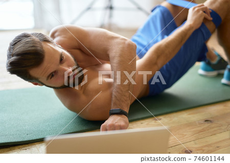 Athletic young man using laptop during home workout 74601144