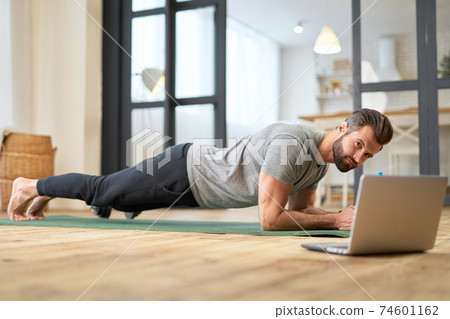 Athletic young man using laptop and doing exercise at home Athletic young man using laptop and doing exercise at home 74601162
