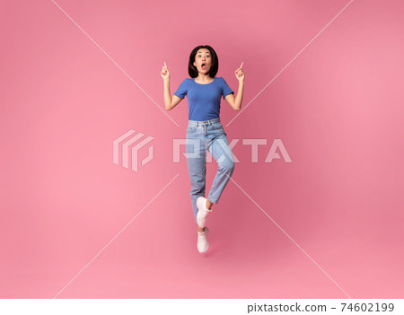 Surprised young asian woman jumping and pointing up Surprised young asian woman jumping and pointing up 74602199