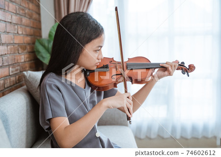 asian girl sitting on sofa holding violin takes out from violin case and testing with violin bow 74602612