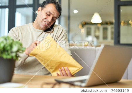 Work at your place. Portrait of hispanic middle aged man talking on the phone while working from home, sitting at the desk with his laptop Work at your place. Portrait of hispanic middle aged man talking on the phone while working from home, sitting at the desk with his laptop 74603149