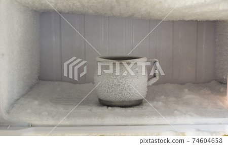Stainless steel drinking water glass in freezer of a refrigerator. Ice buildup inside of a freezer walls. Stainless steel drinking water glass in freezer of a refrigerator. Ice buildup inside of a freezer walls. 74604658