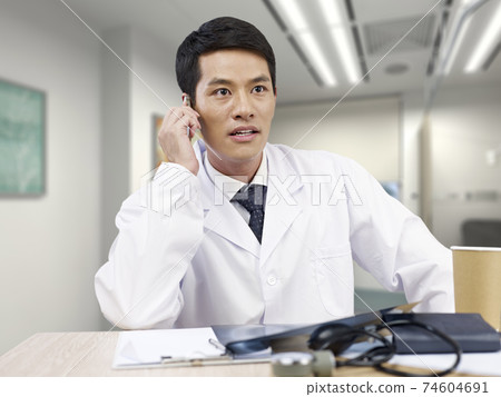 young asian doctor taking a phone call looking shocked young asian doctor taking a phone call looking shocked 74604691