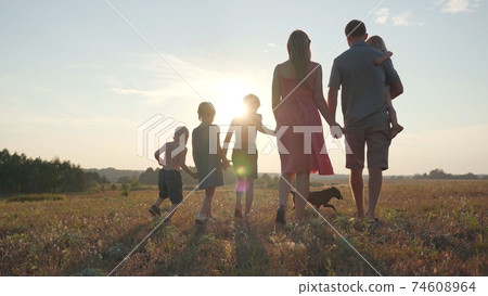 A friendly large family walks across the field at sunset with dog. 74608964