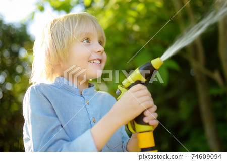 Funny little boy watering plants and playing with garden hose with sprinkler in sunny backyard. Funny little boy watering plants and playing with garden hose with sprinkler in sunny backyard. 74609094